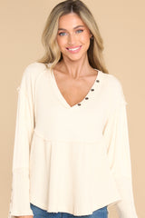 This ivory top features a v-neckline with button detailing, a waffle knit material, button detailing on the sleeves, a pleated peplum style, and an uneven hem. 