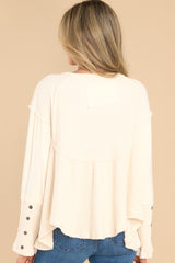 Back view of this top that features a v-neckline with button detailing, a waffle knit material, button detailing on the sleeves, a pleated peplum style, and an uneven hem.