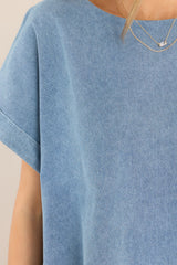 Close up view of this top that features a crew neckline, a denim-like material, and cuffed short sleeves.