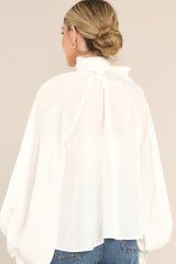 Back view of  this top that features a high neckline, balloon sleeves with buttons at the cuff, an adjustable self tie around the neck, and a flowy fit.