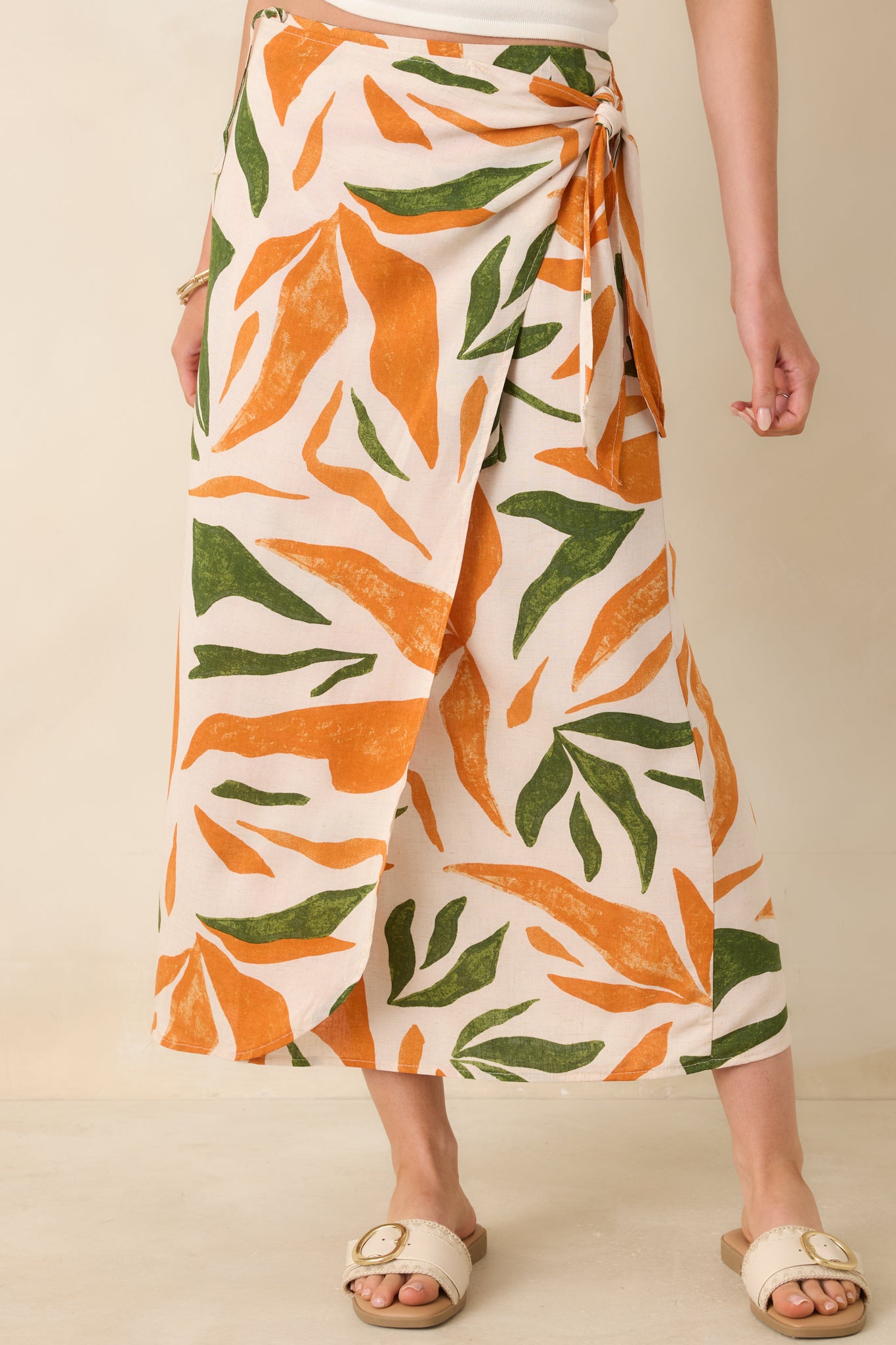 Side view of this tropical print midi skirt that features a high waisted design, an elastic waist insert, self-tie wrap features, an orange & green tropical print, and a lightweight fabric.