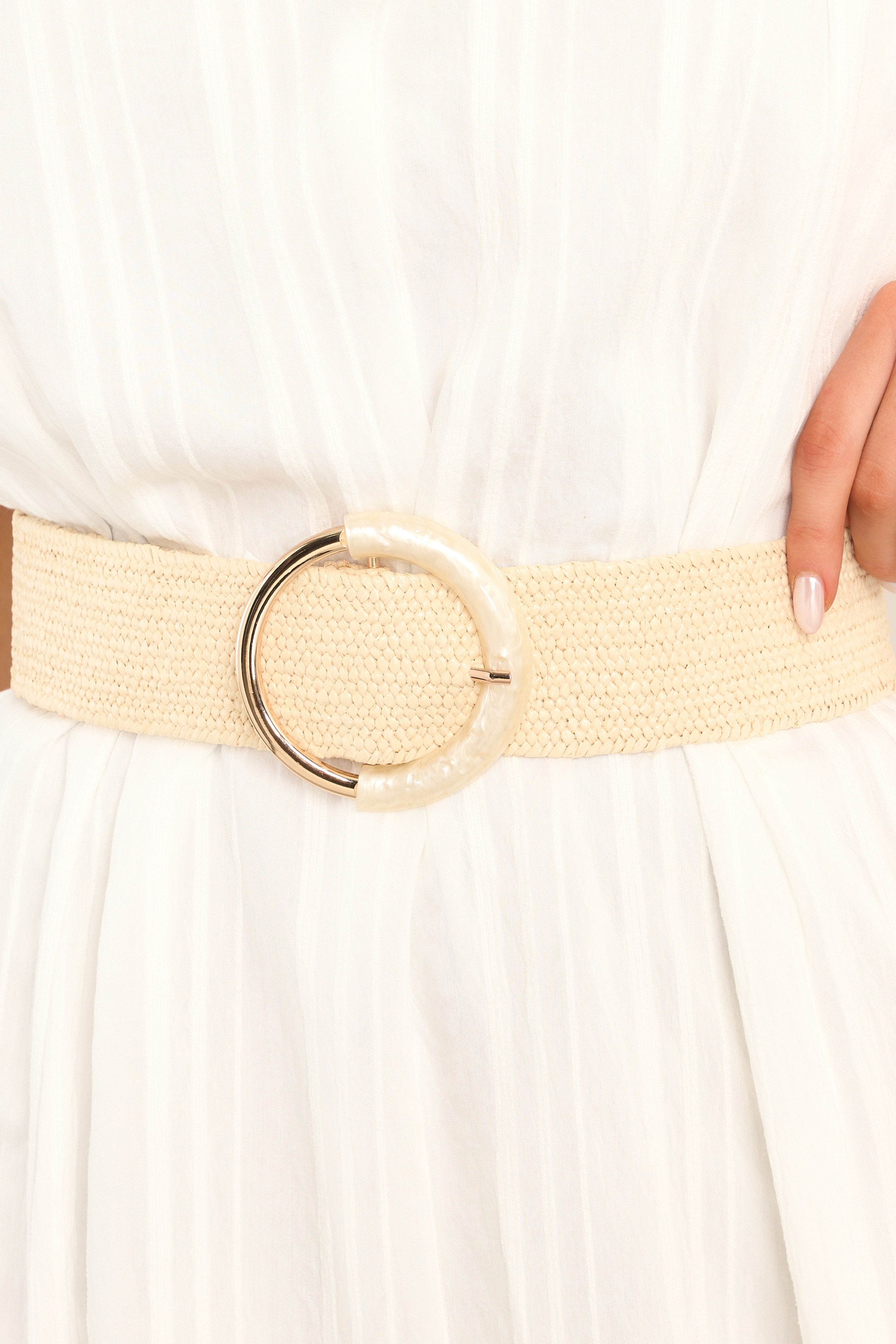 This ivory belt features an elastic band, gold hardware, and a circular buckle with an acrylic accent. 