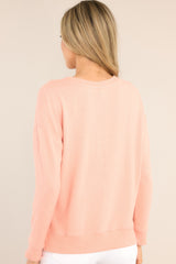 Back view of this top that features a split bottom hem, a ribbed crew neckline, ribbed sleeve cuffs, and a soft peach colored fabric.