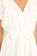 Close up view of this dress that features a v-neckline with ruffle detailing and a self-tie feature, and a self-tie waist belt.
