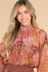 This rust colored multi print top features a high elastic neckline, balloon-like sleeves, elastic cuffs, and ties into a bow at the back of neck with a keyhole opening.