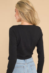 Back view of this top that features a high round neckline, long sleeves, and a cropped hem with a gold ring and twisted fabric detailing.