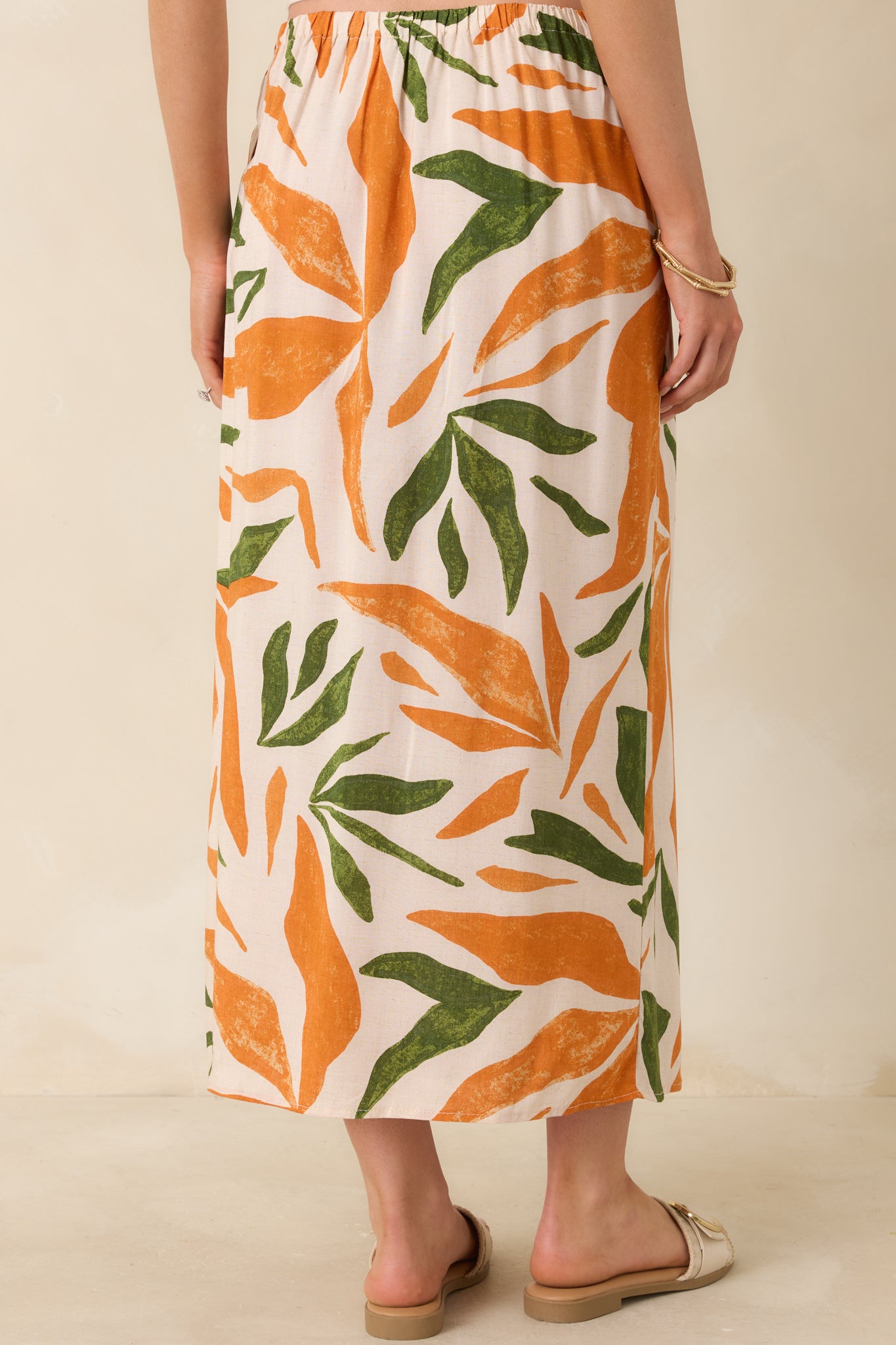 Back view of this tropical print midi skirt that features a high waisted design, an elastic waist insert, self-tie wrap features, an orange & green tropical print, and a lightweight fabric.