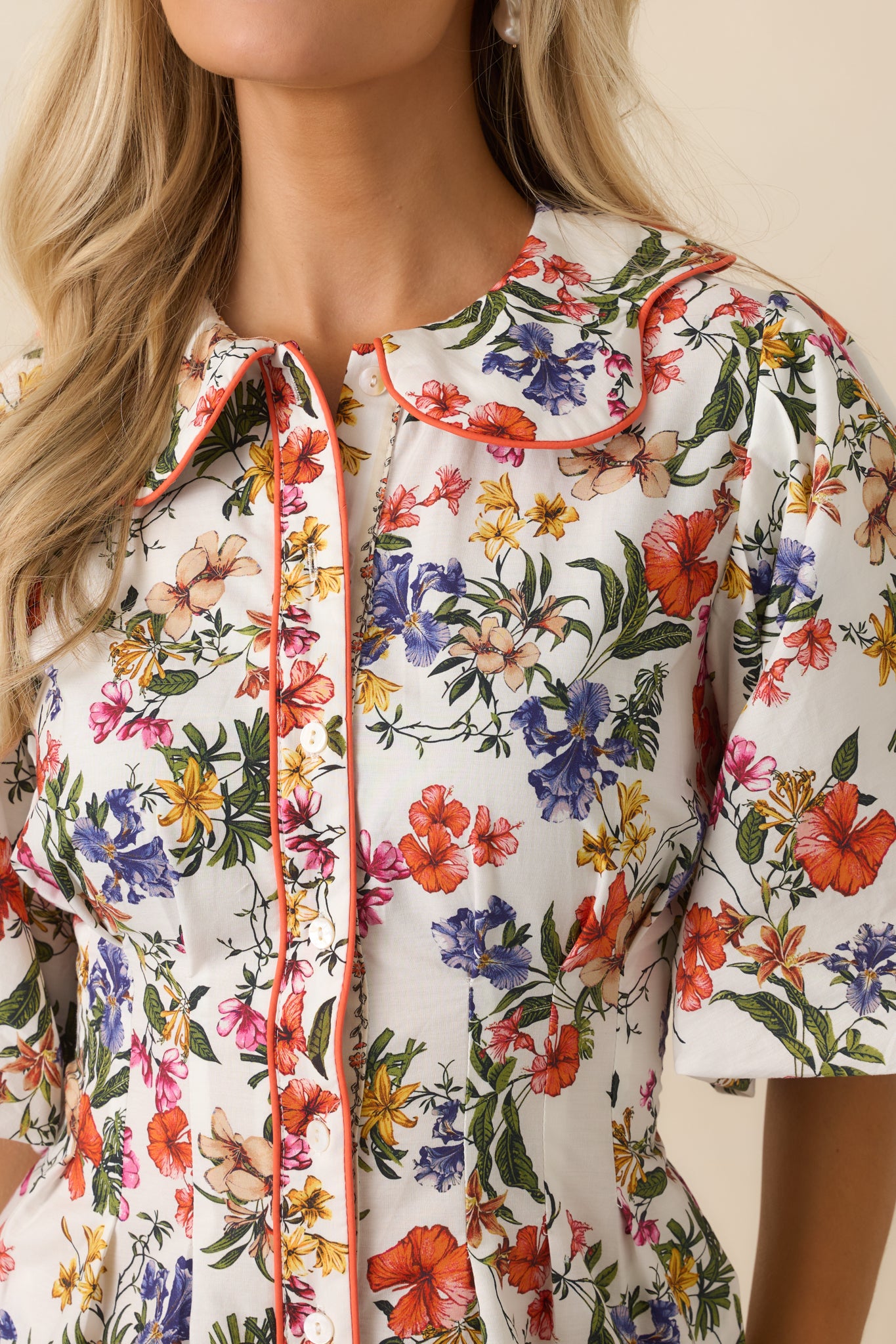 Ivory floral mini dress highlighting the scalloped collar and functional button-front closure framed by vivid orange piping accents.