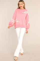 This pink sweatshirt features a crew neckline, dropped shoulders, textured whimsical heart detailing, ribbed cuffed bishop sleeves, and a ribbed hemline. 