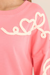 Close up view of this sweatshirt that features a crew neckline, dropped shoulders, textured whimsical heart detailing, ribbed cuffed bishop sleeves, and a ribbed hemline. 