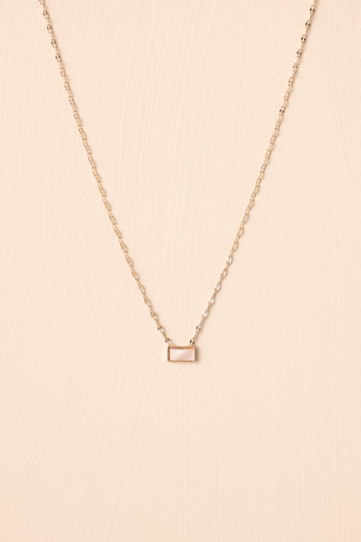 Flat lay of the necklace against a beige surface, emphasizing the adjustable lobster clasp closure and the smooth pearlescent pendant