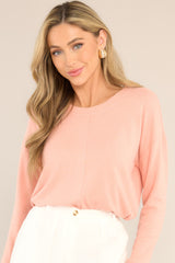 Front view of this top that features a split bottom hem, a ribbed crew neckline, ribbed sleeve cuffs, and a soft peach colored fabric.