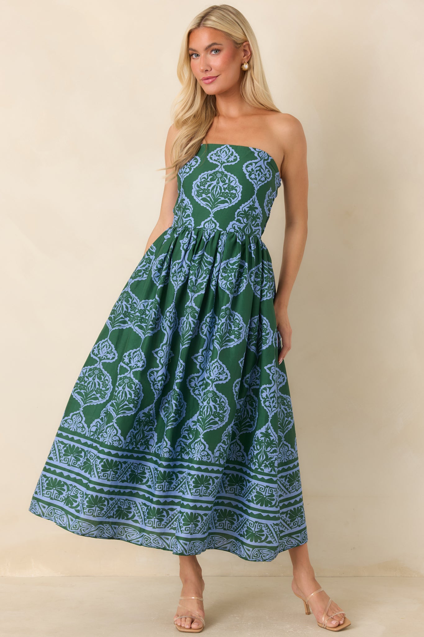 A woman modeling a strapless midi dress with a green and blue paisley block print pattern, standing against a plain beige background.