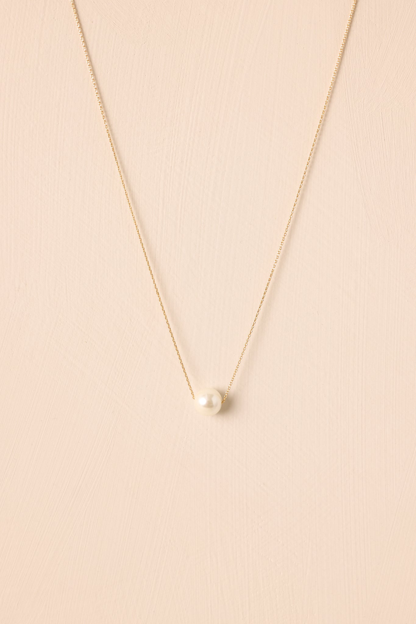 A cropped view of the delicate gold chain necklace featuring a single ivory faux pearl pendant.