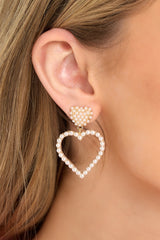 These pearl and gold earrings feature gold hardware, a faux pearl embellished heart shaped stud, a faux pearl heart pendant, and secure post backings. 