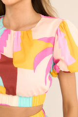 Close up view of this top that features a round neckline, a keyhole cutout at the back of the neck with a button closure, puff sleeves with elastic cuffs, a cutout at the back of the waist, and an elastic waistband.