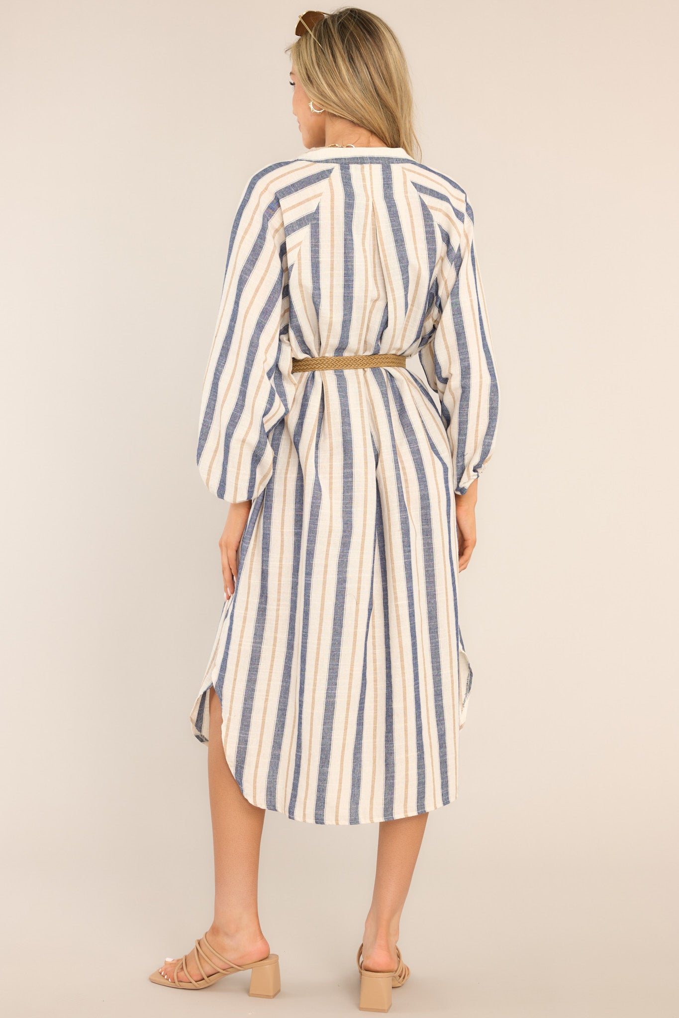 Back view of this dress that features a v-neckline, belt loops, an adjustable belt, functional pockets, elastic cuffed long sleeves, and a vertical striped pattern.
