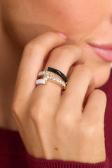 Close-up view of model wearing ring that features gold hardware, black and white accents, rhinestone detailing, and elastic under the band.