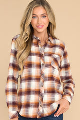 This orange plaid top features a collared neckline, buttons down the front, a front pocket on the bust, and buttons at the cuff.