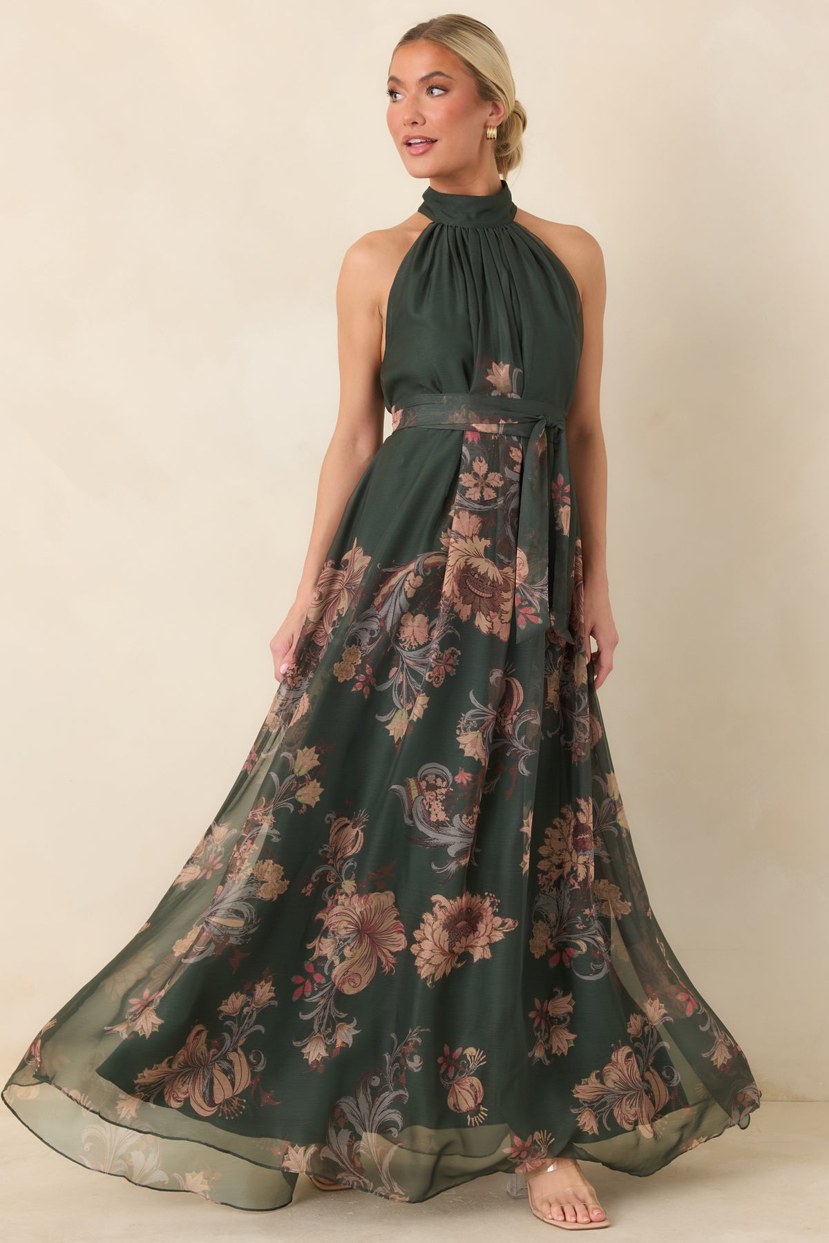 Forest green floral maxi dress with a gathered halter neckline, coordinating waist sash, and flowing sheer overlay skirt.