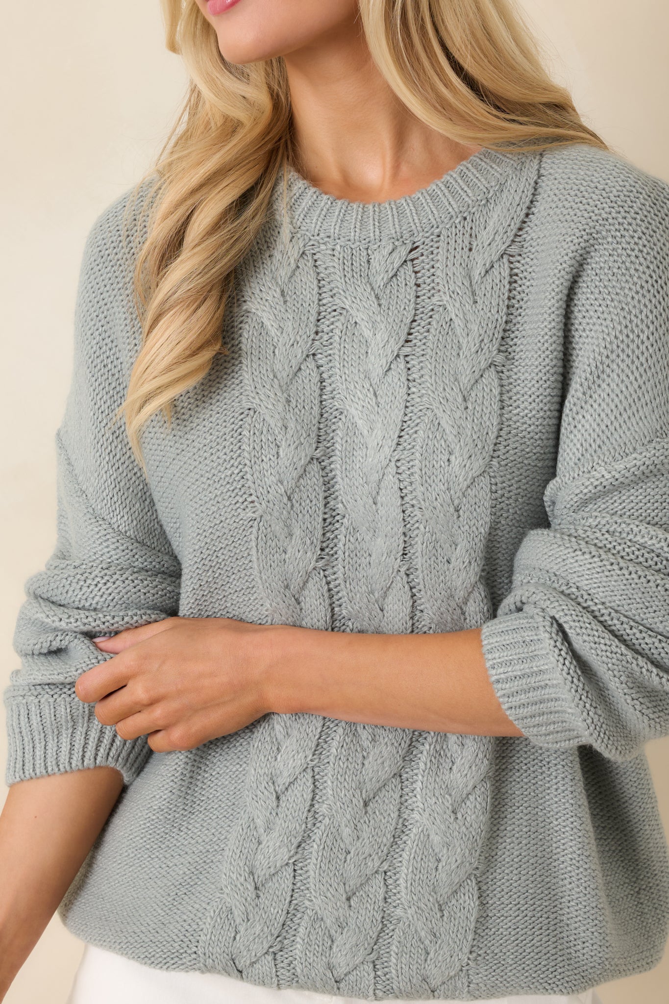 Tight detail of the cable knit texture and ribbed trim on the stone blue sweater, showing the layered stitch work.