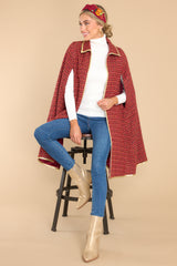 This red cape features a collar neckline with an adjustable gold bow, gold trim detailing, two functional pockets, and tweed fabric.