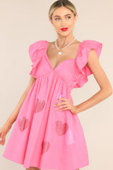 This pink dress features a sweetheart neckline, flutter sleeves, rhinestone heart detailing, functional pockets, and a self-tie bow and zipper in the back. 