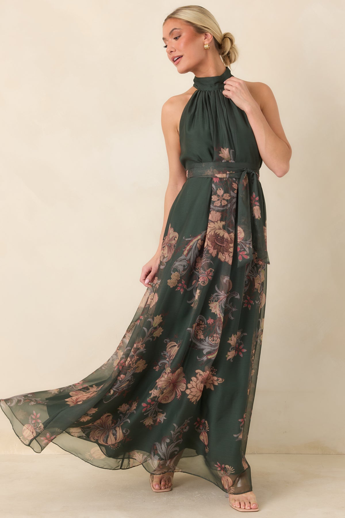 Muted blush, tan, burgundy, and gray florals decorate the deep green maxi dress with a draped bodice and sweeping skirt.