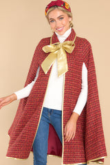 Front view of this cape that features a collar neckline with an adjustable gold bow, gold trim detailing, two functional pockets, and tweed fabric.