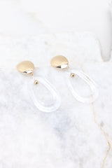 Angled top view of earrings featuring a reflective gold stud with a clear loop dangle, as well as a secure post backing