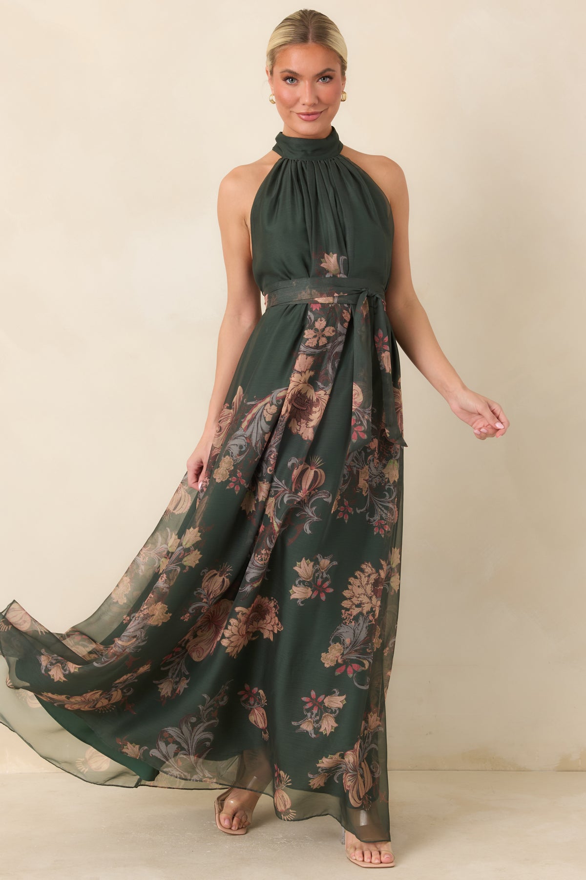 A draped halter neckline and coordinating sash complement the ornate floral print and floor-length skirt of this green dress.