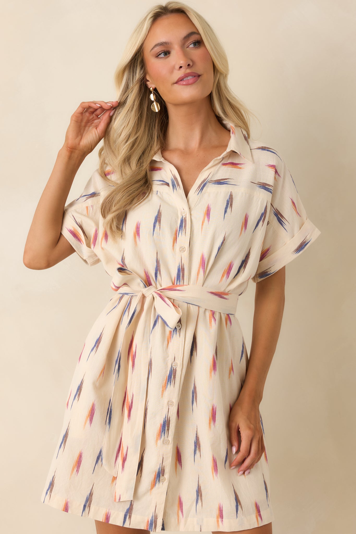 Cream shirt dress featuring side pockets and a relaxed button-front design with colorful abstract print.