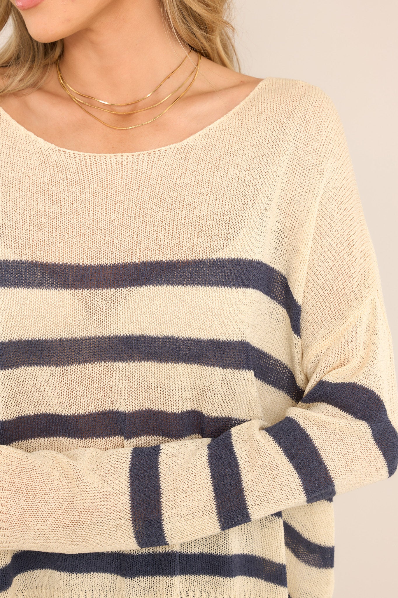 Close up view of this sweater that features a wide crew neckline, dropped shoulders, a lightweight knitted material, classic stripes, and long sleeves. 