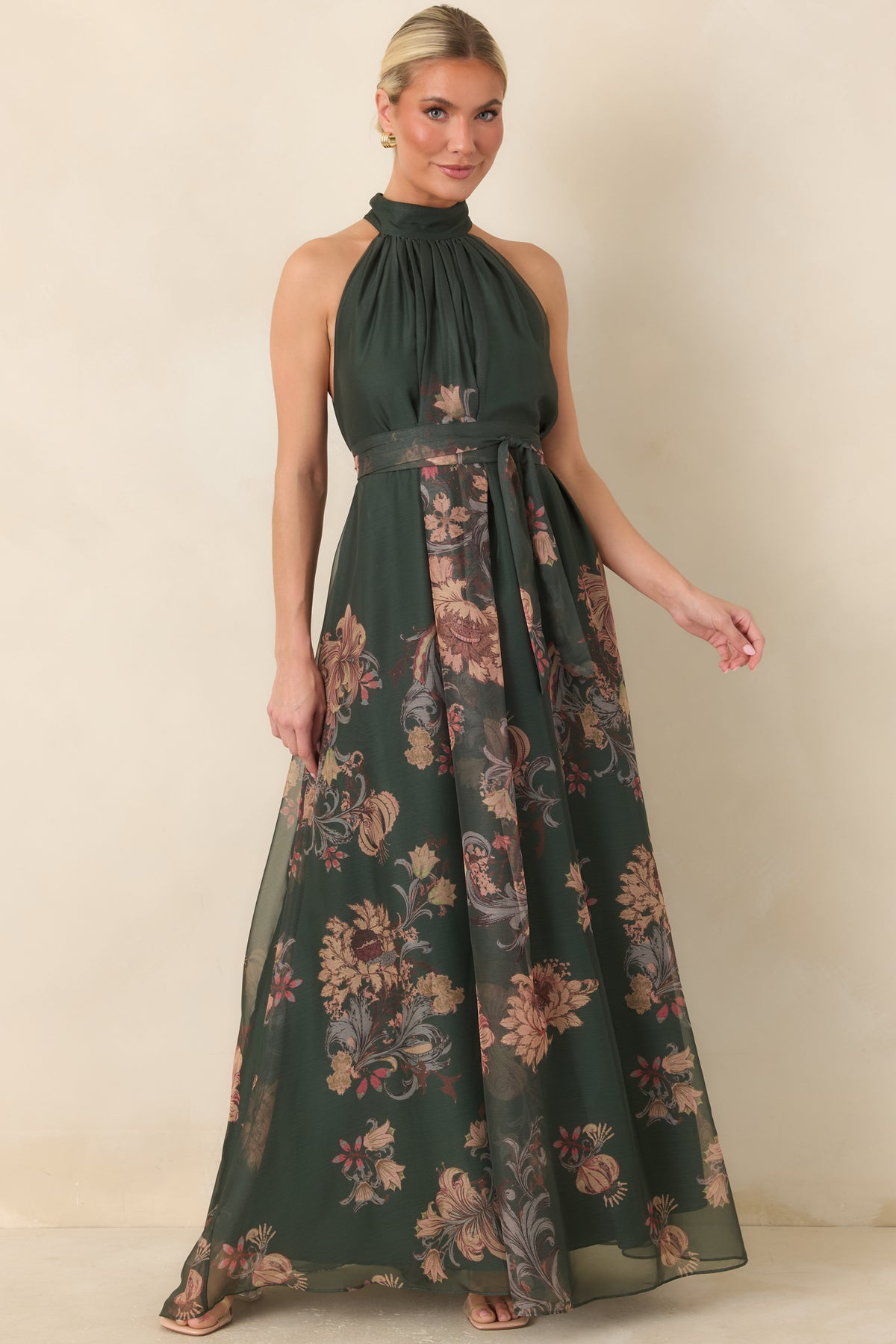 Muted burgundy, blush, tan, and gray botanicals stand out against the deep green dress, with a flowing overlay creating a layered maxi silhouette.