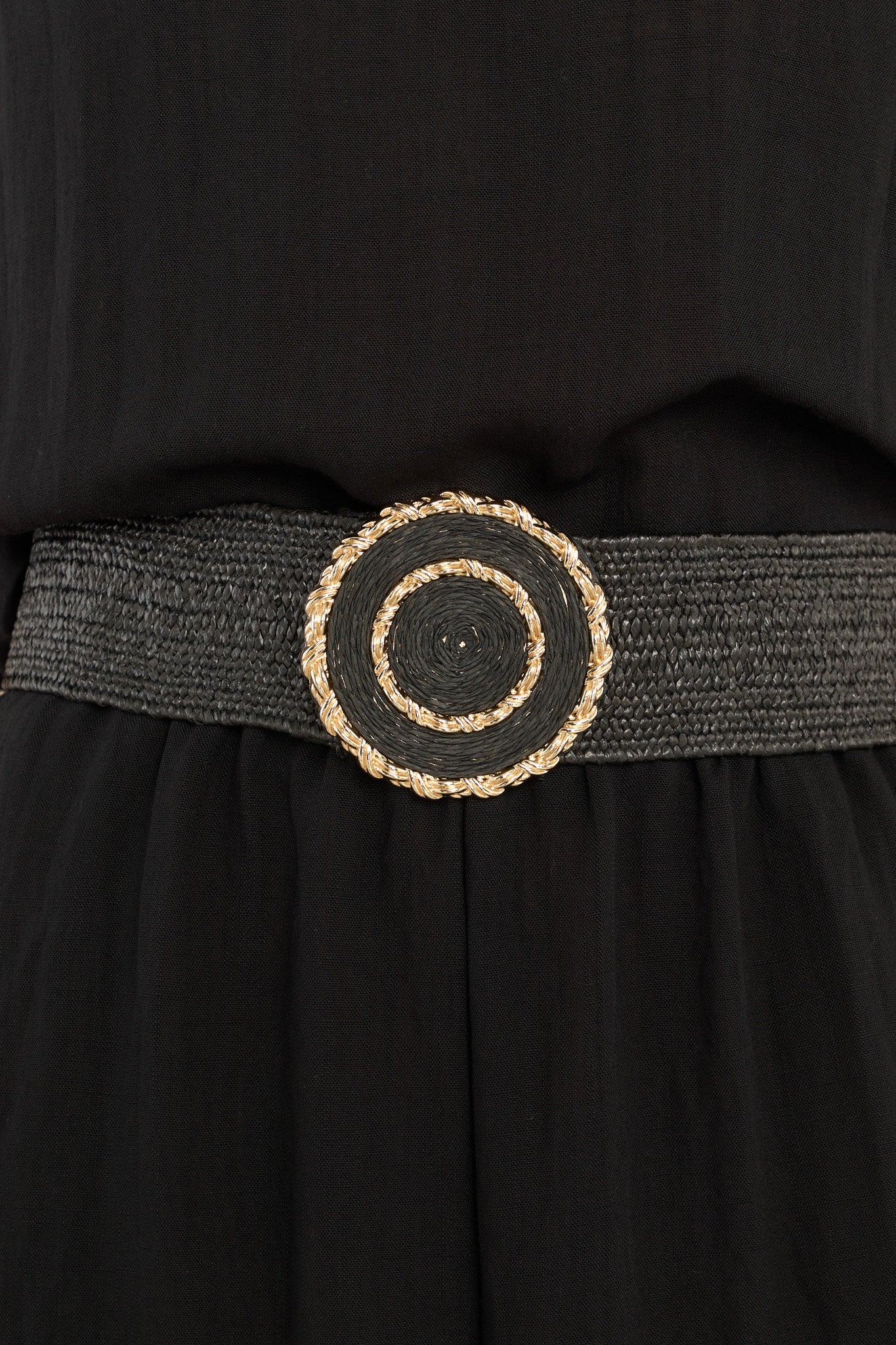 This black belt features gold hardware, an elastic band, a circular design, and a hook and bar closure.