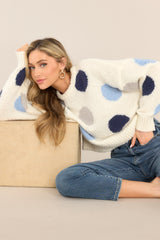 Cozy, long sleeve ivory sweater, with navy blue, periwinkle, and soft grey, large polka dots. It also has a ribbed hemline and cuffs.