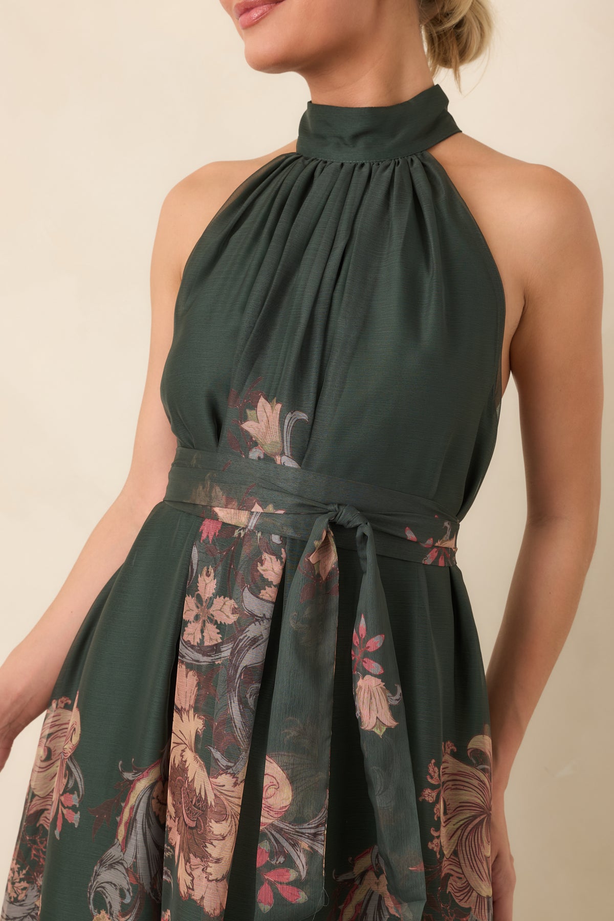 Close-up of the forest green floral dress highlights the gathered halter neckline, softly draped bodice, and muted botanical print.