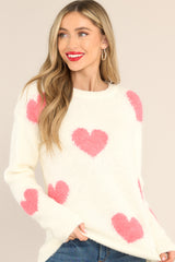 Front view of this sweater that showcases the pink heart pattern of the ivory fabric.