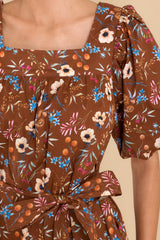 Close up view of this dress that features a square neckline, puffed sleeves, a self-tie belt, functional pockets, and a floral pattern.