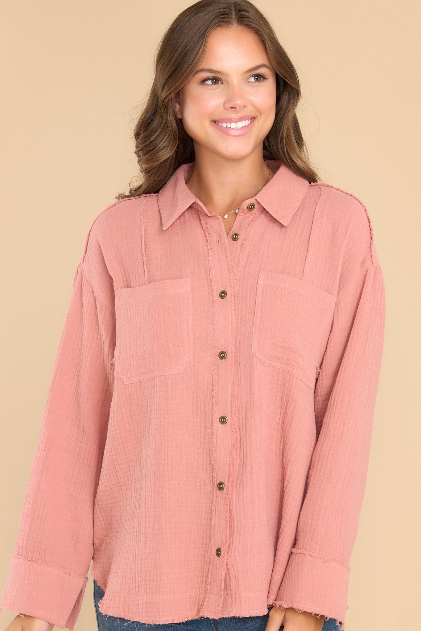 This blush pink top features a collared neckline, buttons down the front, and two pockets on the bust.