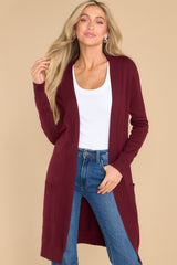 This burgundy cardigan features an open front accompanied by ribbed details, straight long sleeves, and functional front pockets.