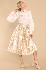 This gold skirt features a high waist, raised gold flower details, waist pockets, a hemmed bottom, and a back zipper closure.