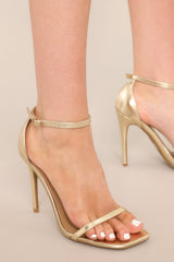 Close up view of gold high heel sandals featuring gold hardware on the adjustable strap and heel measurement of 4.5