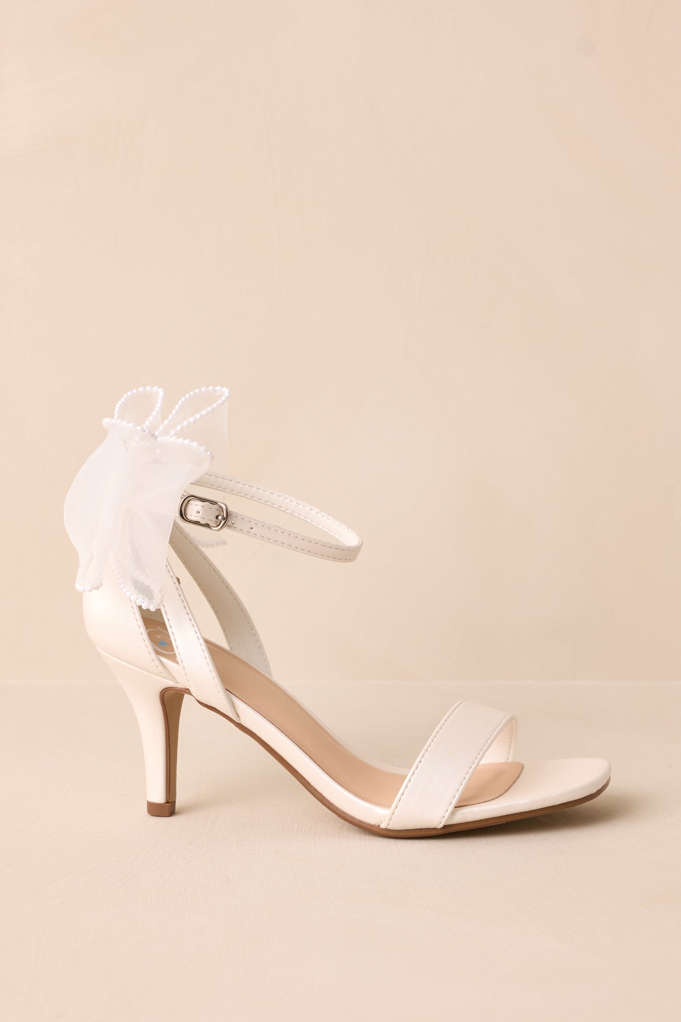 Close-up side view of the white heels, showcasing the contrast between the white toe strap and the elegant ivory lace bow with pearls on the heel.