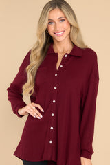 This burgundy top features button-down closures on the front, a collared neckline, cuffed sleeves, and a chest pocket. 
