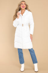 Full view of puffed, knee length white coat featuring a high neckline and hood, a functional zipper down the front, an elastic belt, and pockets with zipper closures.