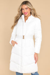 Front view of puffed, knee length white coat featuring a high neckline and hood, a functional zipper down the front, an elastic belt, and pockets with zipper closures.