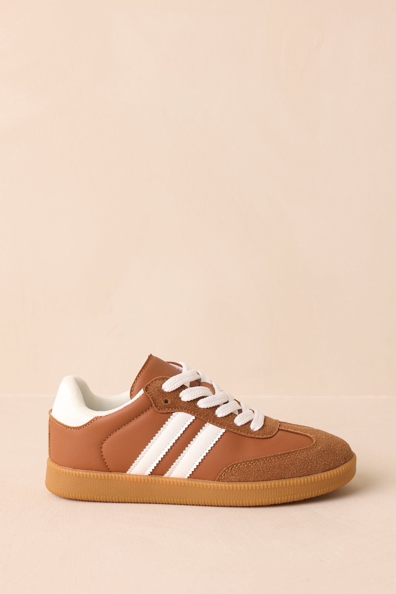 A side angle of caramel brown low-top sneakers showing faux leather and faux suede upper with contrast white stripes and a gum rubber outsole.