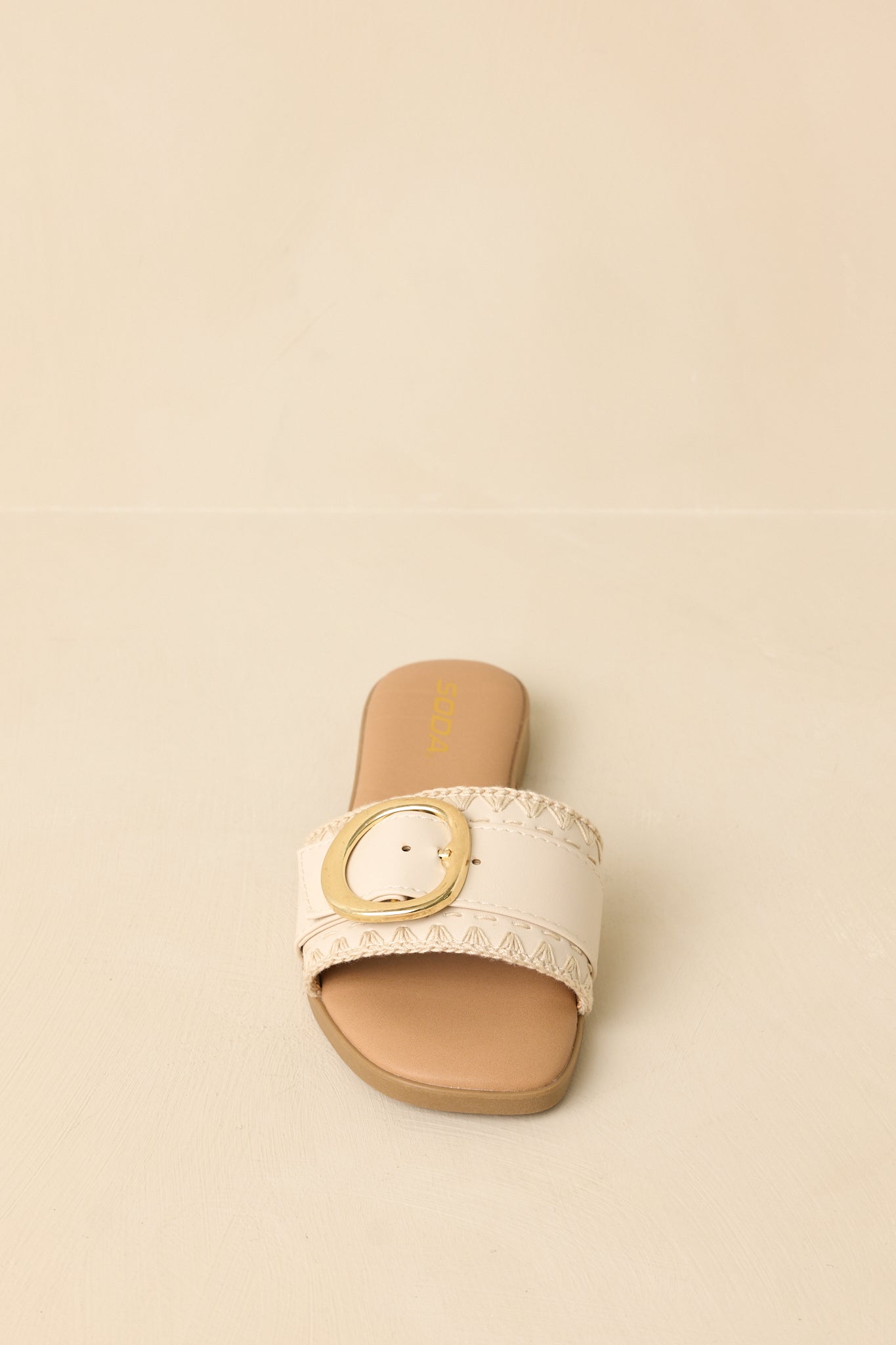Beige faux leather slides angled to emphasize the structured strap and polished buckle.