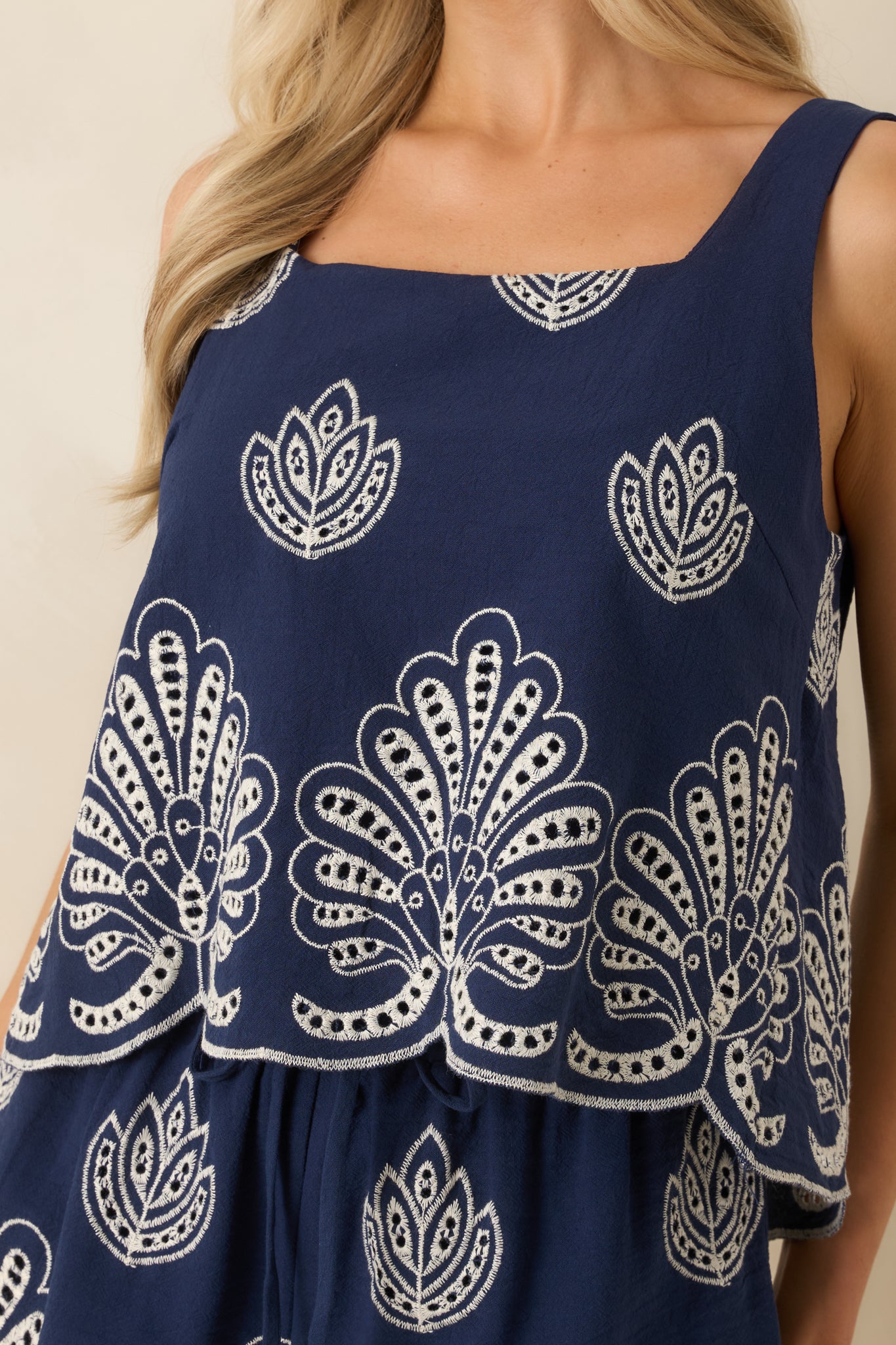 Detailed view of scalloped embroidery and cotton texture on the navy tank hem.